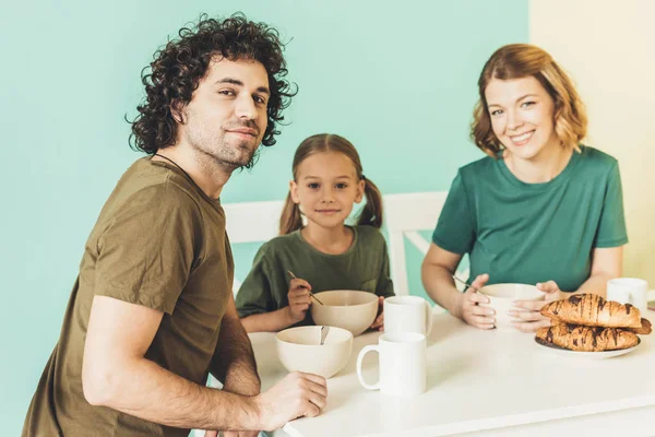 Feliz familia desayunando juntos y sonriendo a la cámara - foto de stock