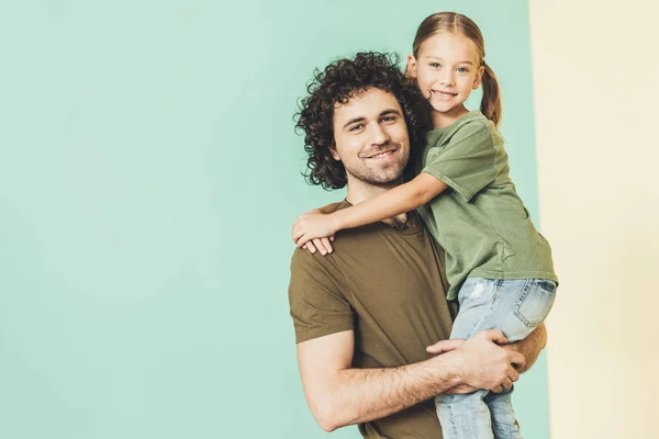 Feliz padre llevando adorable hijita y sonriendo a la cámara - foto de stock