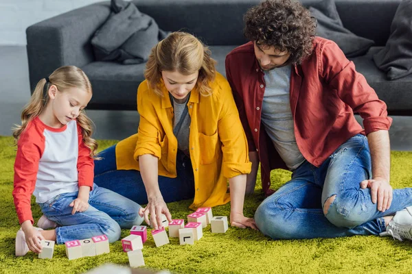 Genitori felici e carina figlioletta che gioca con blocchi di legno a casa — Foto stock