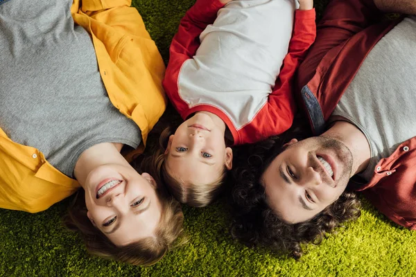 Vista superior da família feliz com uma criança deitada juntas e sorrindo para a câmera — Fotografia de Stock