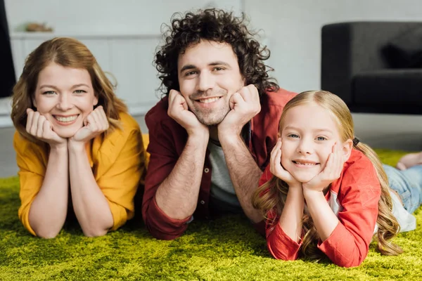 Familia feliz con un niño acostado juntos y sonriendo a la cámara - foto de stock