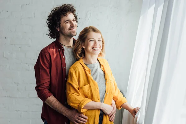 Schönes glückliches Paar, das sich umarmt und zum Fenster blickt — Stockfoto