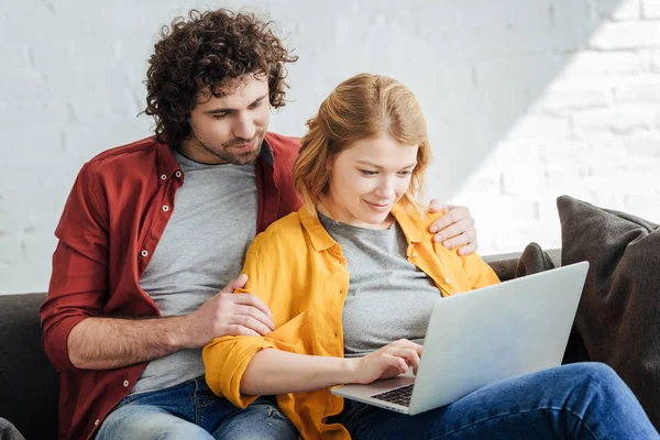 Pareja joven sentada en el sofá y el uso de ordenador portátil juntos en casa - foto de stock