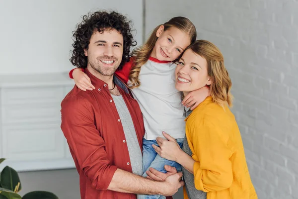 Happy parents with adorable little daughter hugging and smiling at camera — Stock Photo