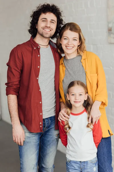 Feliz joven familia de pie juntos y sonriendo a la cámara - foto de stock