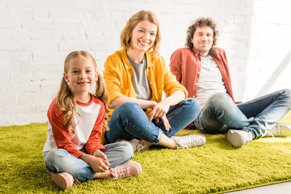 Pais felizes com adorável filhinha sorrindo para a câmera enquanto sentados juntos — Fotografia de Stock