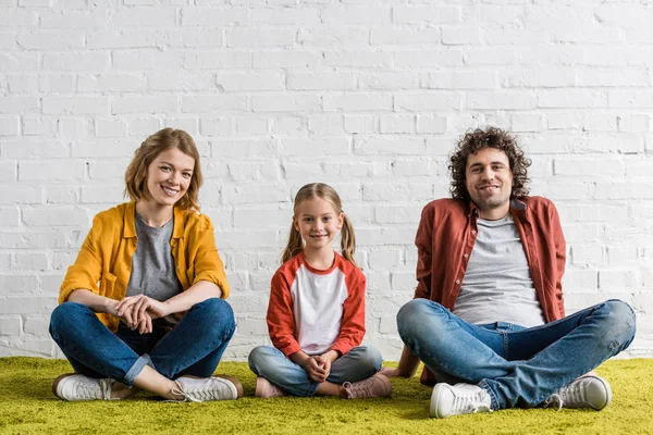 Famille heureuse avec un enfant souriant à la caméra tout en étant assis ensemble — Photo de stock