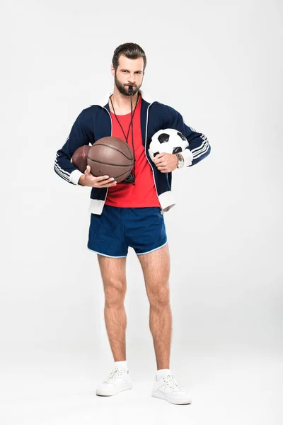 Entrenador deportivo con silbato que sostiene pelotas de rugby, baloncesto y fútbol, aislado en blanco - foto de stock