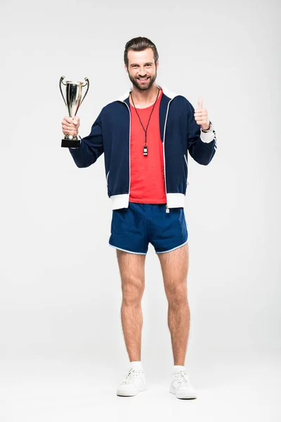 Entrenador deportivo feliz con copa de trofeo mostrando el pulgar hacia arriba, aislado en blanco - foto de stock