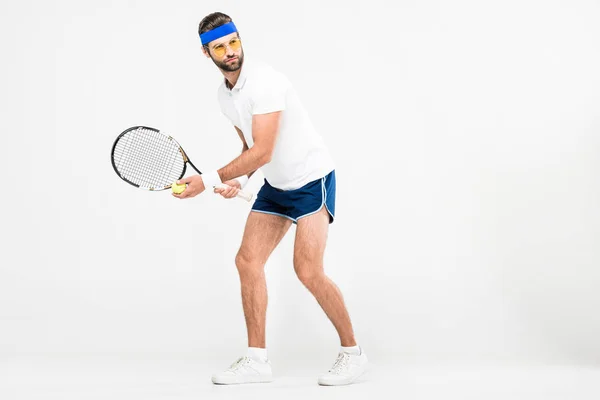 Hombre guapo en gafas de sol retro jugando al tenis con raqueta y pelota, aislado en blanco - foto de stock