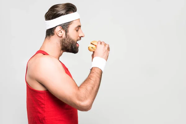 Бородатый спортсмен ест гамбургер, изолированный на белом — стоковое фото