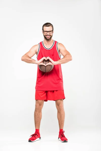 Jugador de baloncesto sonriente con bola que muestra el símbolo del corazón, aislado en blanco - foto de stock