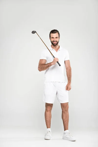 Golfeur masculin joyeux en tenue de sport blanche avec club de golf, isolé sur gris — Photo de stock