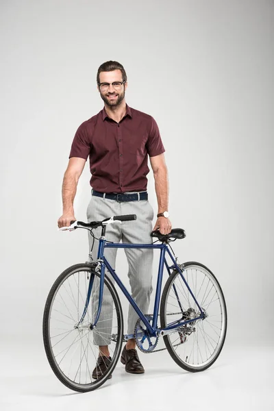 Elegante uomo sorridente in posa con bicicletta, isolato su grigio — Foto stock