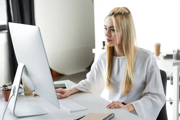 Schöne junge blonde Frau arbeitet mit Desktop-Computer im Büro — Stockfoto