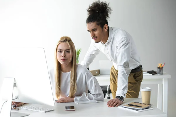 Jovens colegas multiétnicos que olham para o computador desktop enquanto trabalham juntos no escritório — Fotografia de Stock