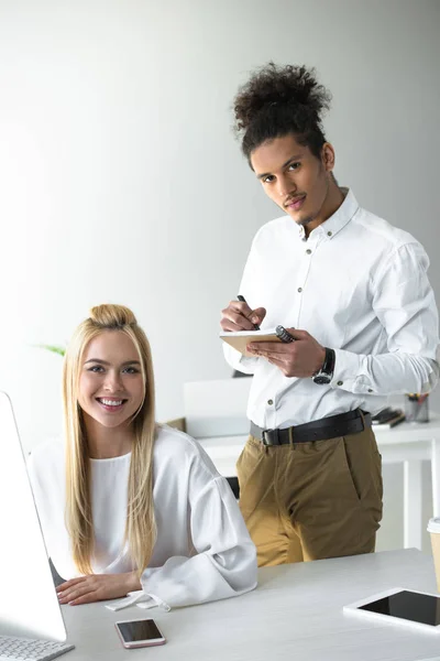 Jóvenes empresarios sonriendo a la cámara mientras trabajan juntos en la oficina — Stock Photo