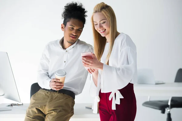 Souriant jeunes collègues utilisant smartphone ensemble dans le bureau — Photo de stock