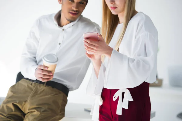 Tiro cortado de jovens colegas de trabalho olhando para smartphone juntos no escritório — Fotografia de Stock