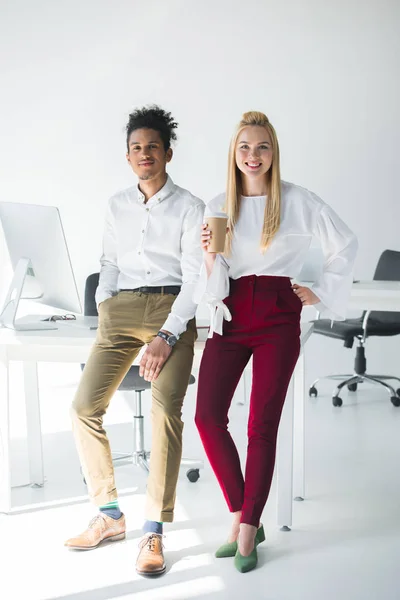 Full length view of young multiethnic business colleagues smiling at camera while standing together in office — Stock Photo