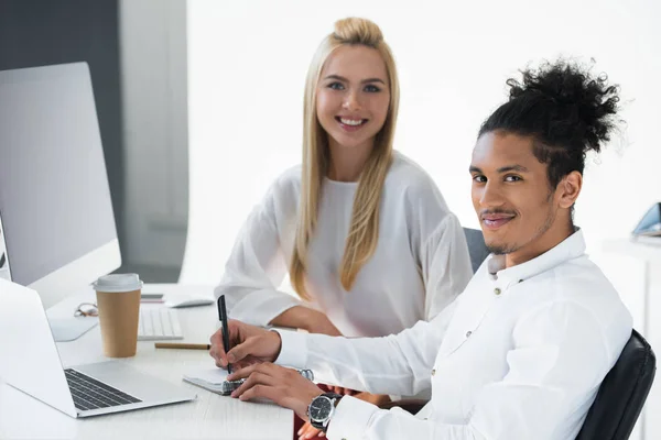 Jeunes collègues d'affaires multiethniques souriant à la caméra tout en travaillant ensemble au bureau — Photo de stock