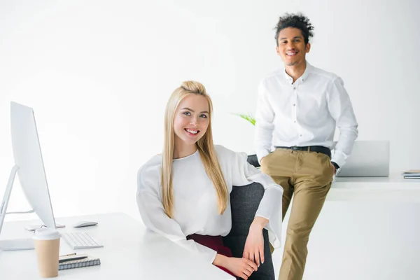Joyeux jeunes gens d'affaires multiethniques souriant à la caméra tout en travaillant ensemble dans le bureau — Stock Photo