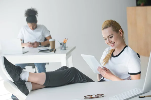 Bella sorridente giovane donna utilizzando tablet digitale sul posto di lavoro — Foto stock