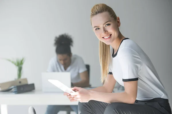 Schöne junge blonde Frau mit digitalem Tablet und lächelnd in die Kamera im Büro — Stockfoto