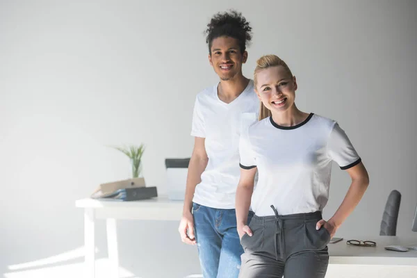 Fröhliche junge multiethnische Kollegen, die im Büro zusammen in die Kamera lächeln — Stockfoto