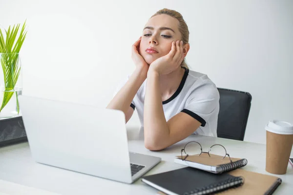 Нудна молода бізнес-леді дивиться на ноутбук, сидячи на робочому місці — стокове фото