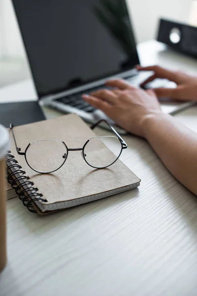 Close-up view of eyeglasses on notebook and person using laptop behind — Stock Photo