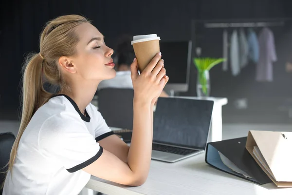 Vista laterale di rilassato giovane donna con gli occhi chiusi in possesso di tazza di carta in ufficio — Foto stock