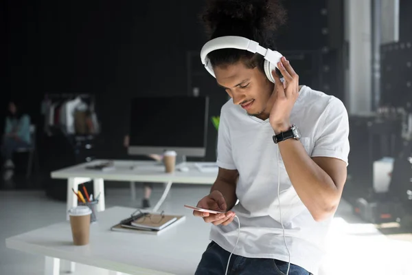 Joven afroamericano hombre en auriculares usando teléfono inteligente en la oficina — Stock Photo
