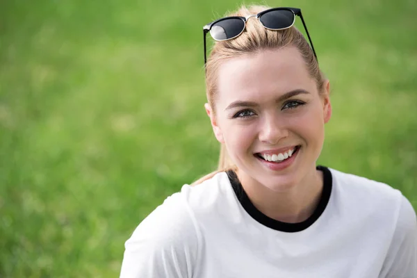 Retrato de hermosa chica rubia con gafas de sol en la cabeza sonriendo a la cámara al aire libre - foto de stock