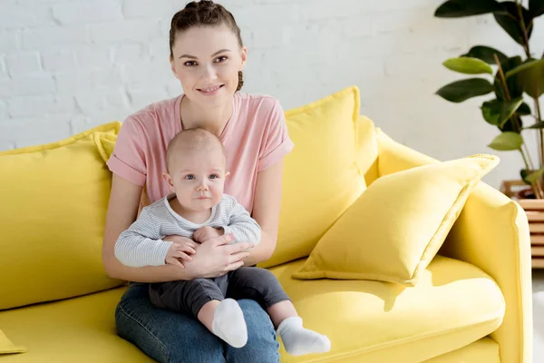 Giovane madre sorridente con piccolo figlio seduto sul divano — Foto stock