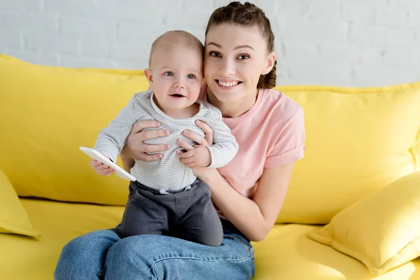 Mãe feliz com o pequeno filho segurando smartphone e sentado no sofá — Fotografia de Stock