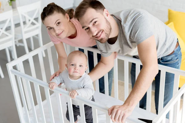 Happy parents with little son in baby crib at home — Stock Photo