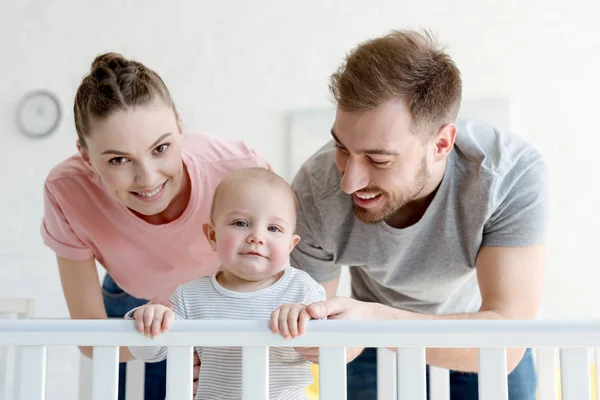 Happy parents with infant boy in baby crib at home — Stock Photo
