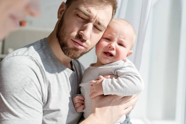 Молодой отец держит плачущего маленького сына — стоковое фото