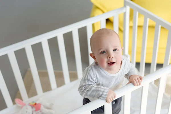 Happy little boy standing in baby crib — Stock Photo