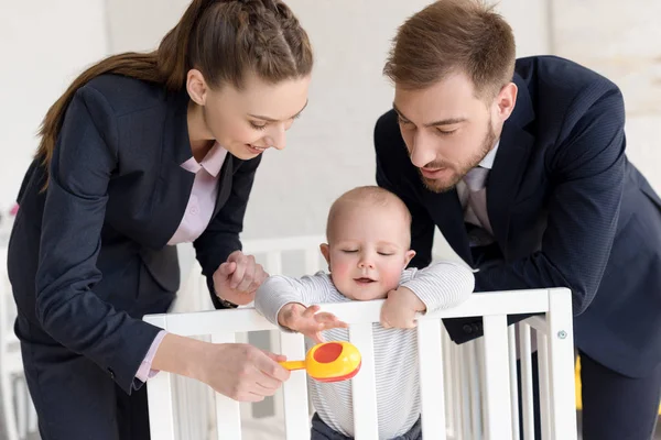 Happy businesspeople playing with little son in baby crib at home — Stock Photo