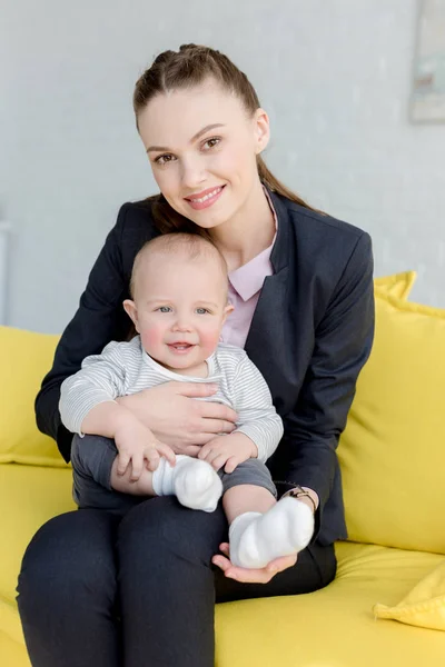 Bela mulher de negócios sorridente sentado no sofá com o pequeno filho — Fotografia de Stock