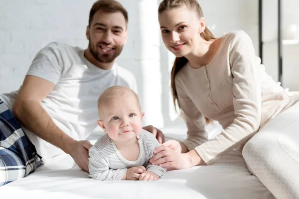 Pais sorridentes com o pequeno filho na cama — Fotografia de Stock