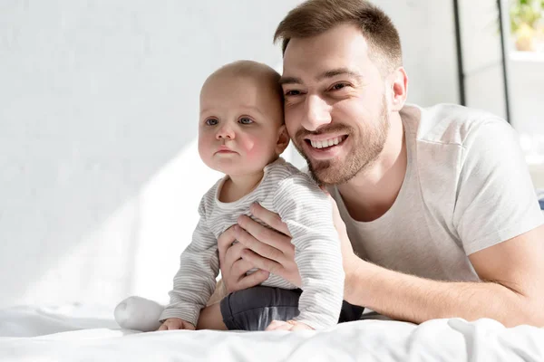Sonriente padre guapo con pequeño hijo acostado en la cama - foto de stock