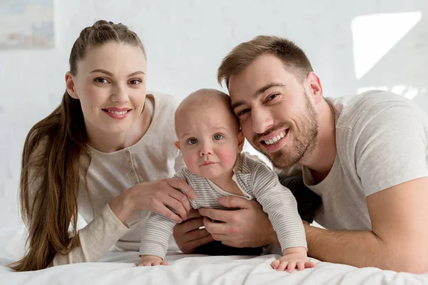 Smiling parents with little boy on bed — Stock Photo