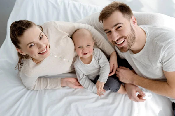 Vue aérienne de jeunes parents heureux avec un bébé couché sur le lit — Photo de stock