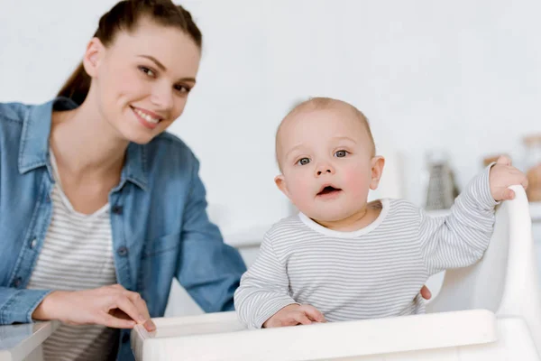 Madre feliz con el niño pequeño sentado en la cocina - foto de stock