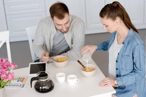 Marido e mulher tomando café da manhã com flocos de milho e café na cozinha com tablet digital — Fotografia de Stock