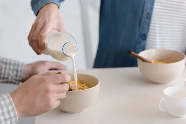 Verter leche en copos de maíz, pareja joven desayunando - foto de stock