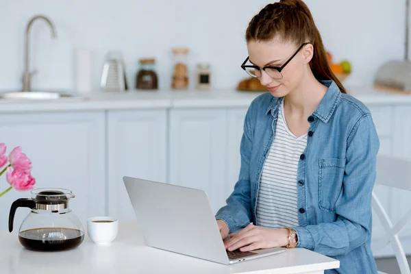 Young female freelancer using laptop on kitchen with coffee — Stock Photo